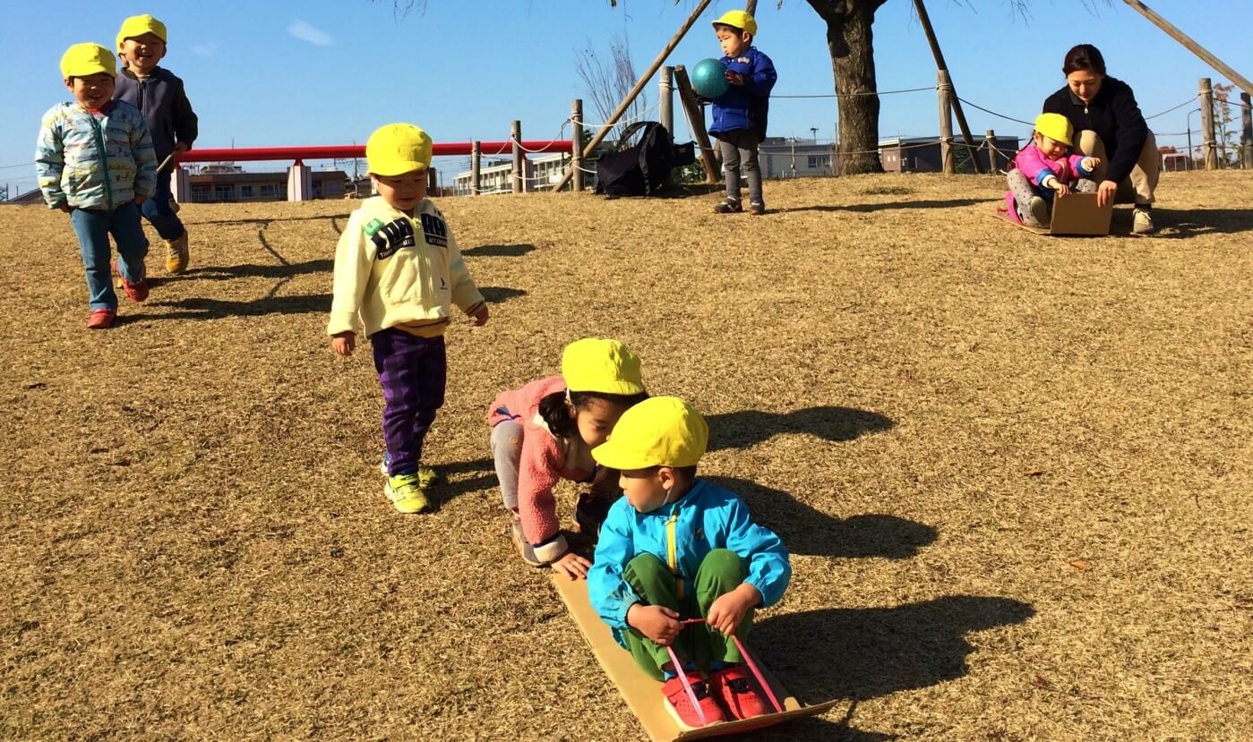 手作りのスライダーで芝生をすべる子どもら