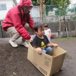 築山を段ボール箱で滑る子ども