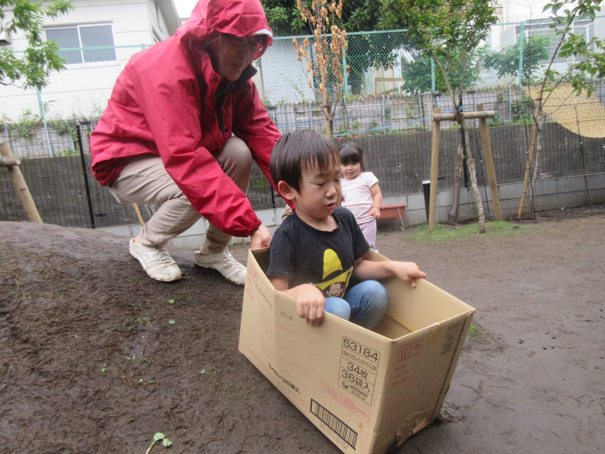 築山を段ボール箱で滑る子ども