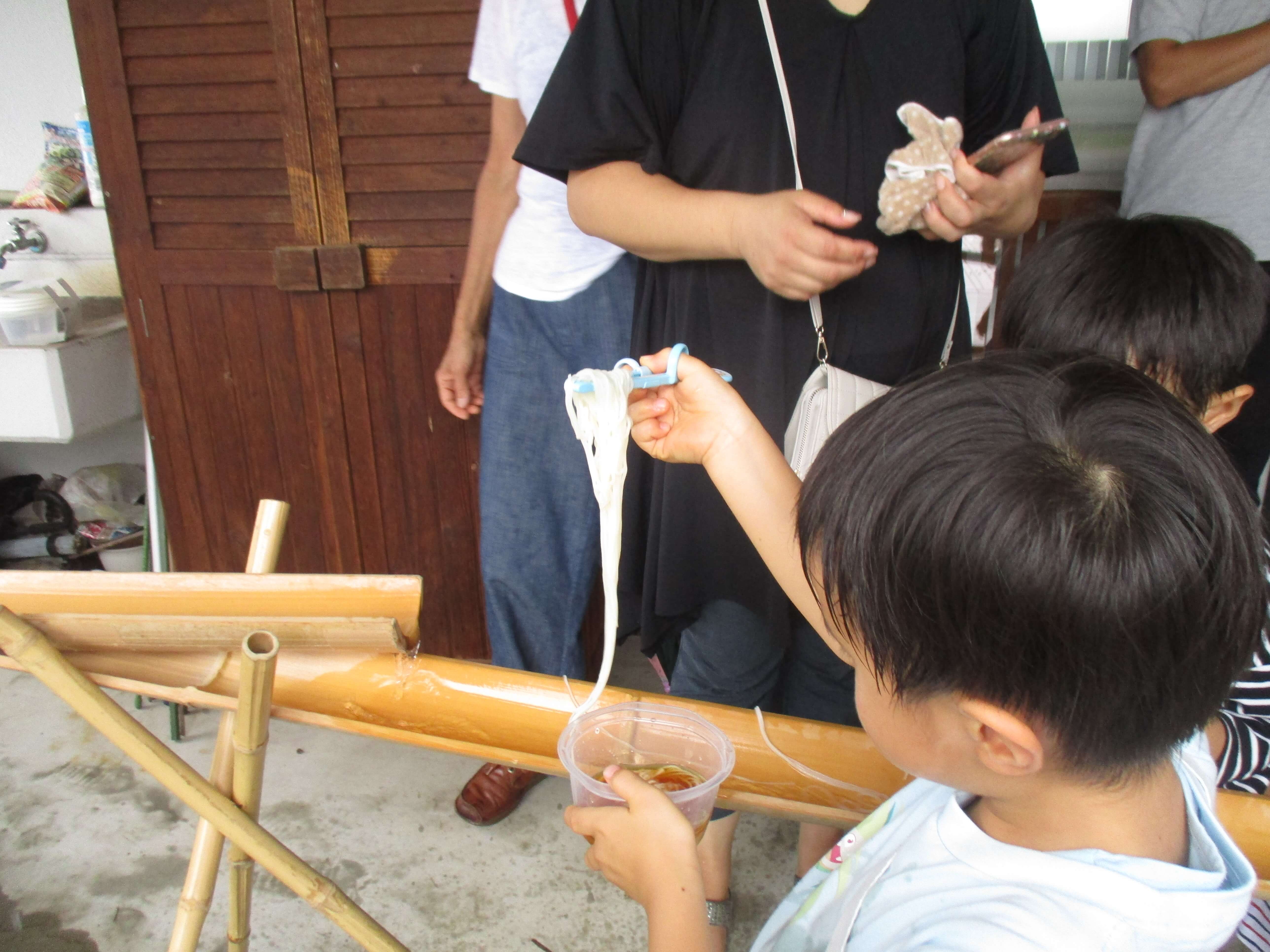 流しそうめんをすくう子ども