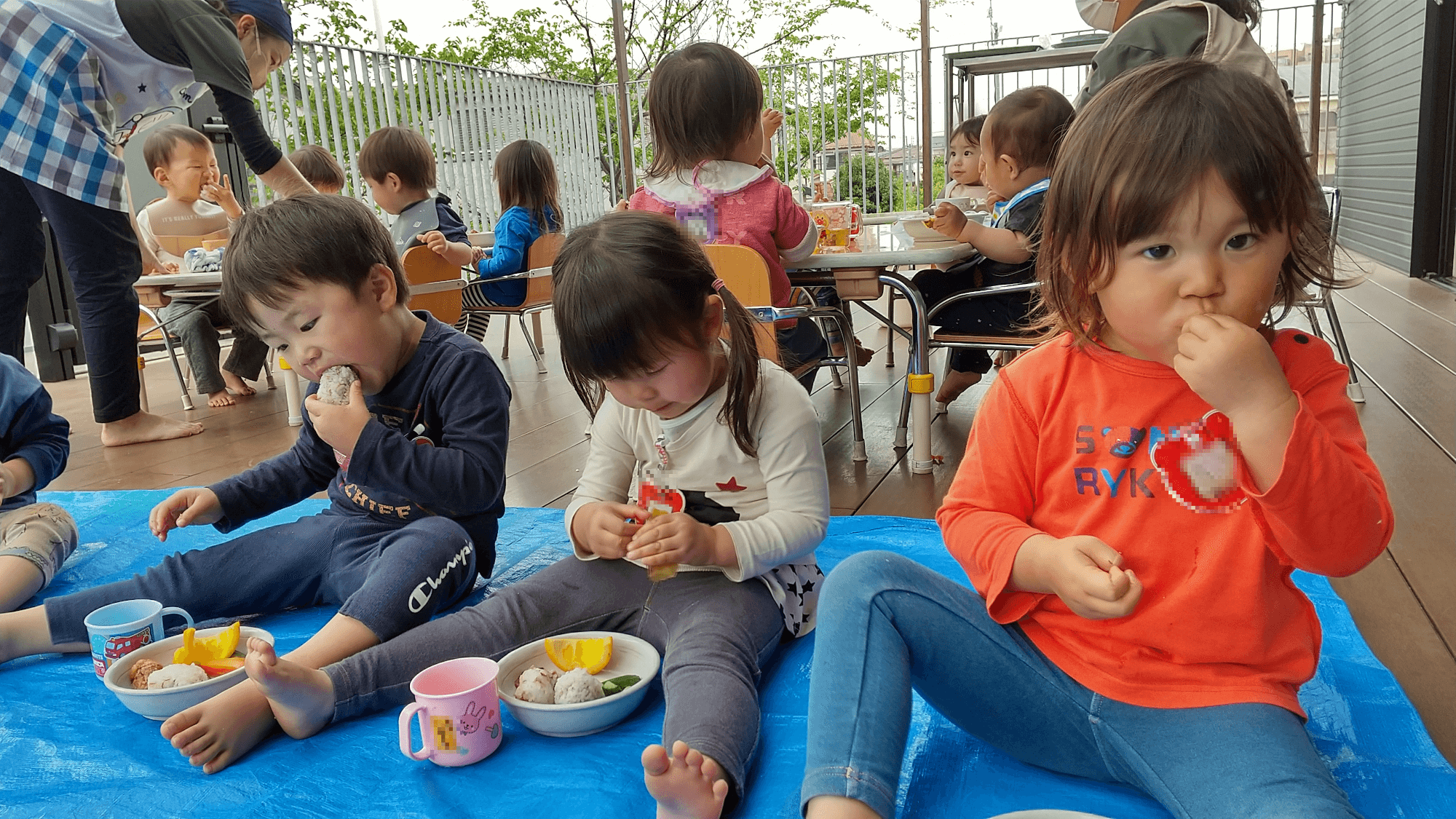 園庭にレジャーシートを引いてお弁当を食べる子どもたち