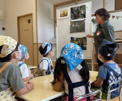 子どもたちに写真を見せながら梅採りでの経験を話す小松さん