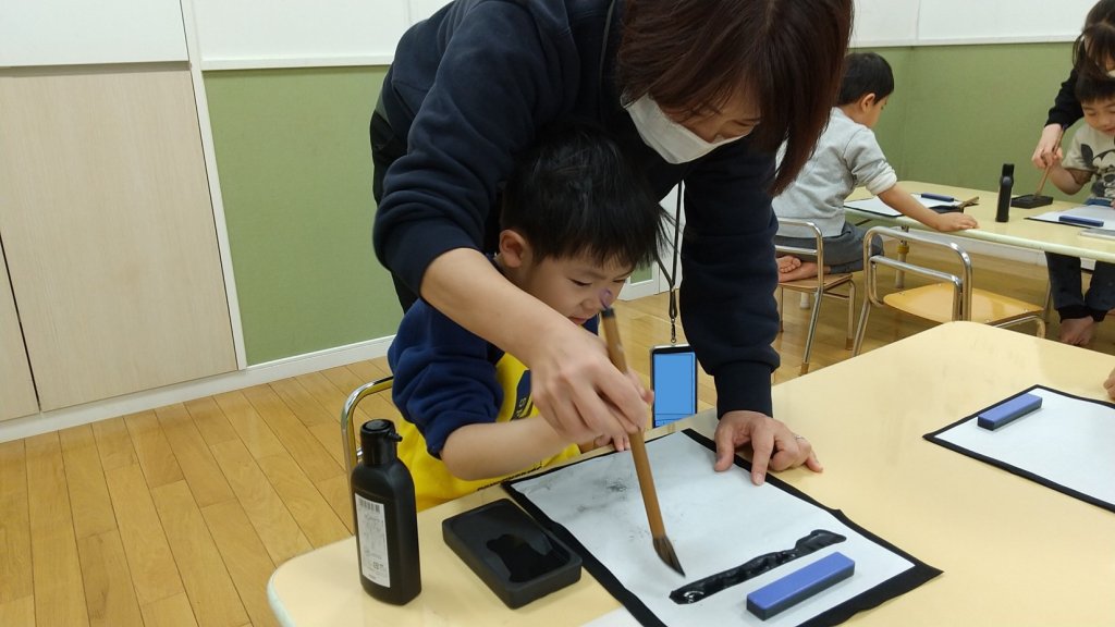 筆の持ち方を教わる子ども